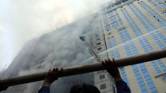 A person looks on as firefighters attempt to extinguish a fire at a multi-storey commercial building in Dhaka