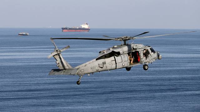 FILE PHOTO: MH-60S helicopter hovers in the air with an oil tanker in the background as the USS John C. Stennis makes its way to the Gulf through the Strait of Hormuz
