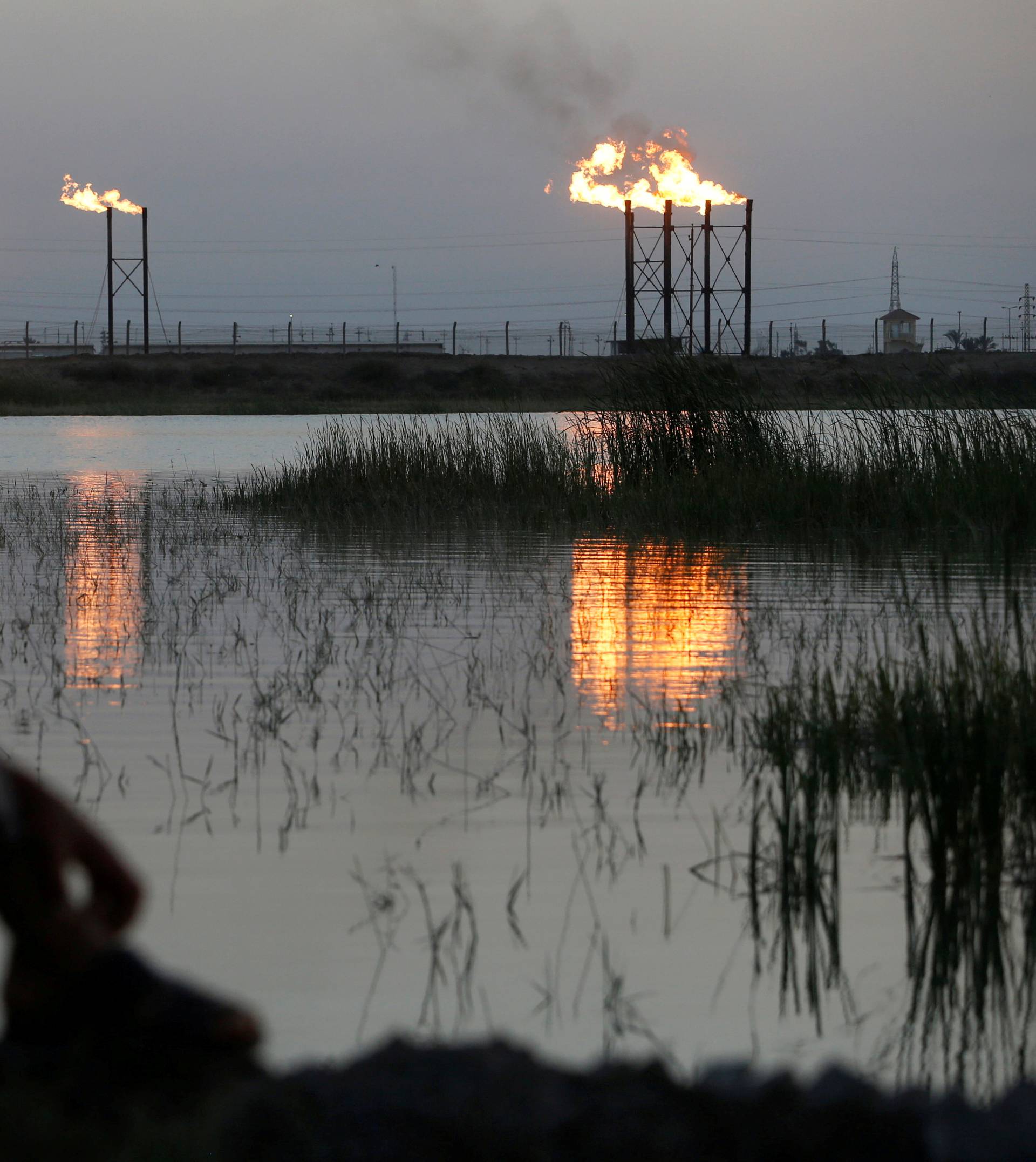 FILE PHOTO: Flames emerge from flare stacks at Nahr Bin Umar oil field, as a man is seen wearing a protective face mask , following the outbreak of the coronavirus, north of Basra