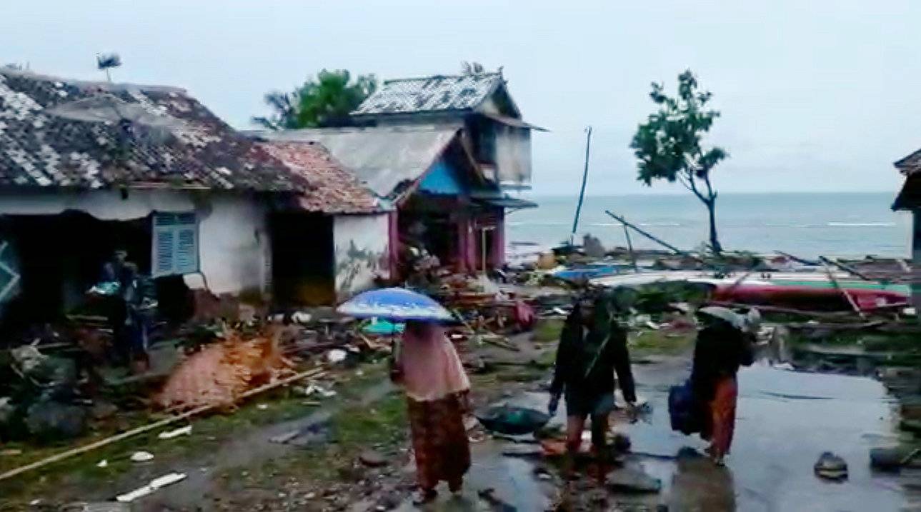 People are seen near the debris surrounding a house damaged by tsunami at Lampung province