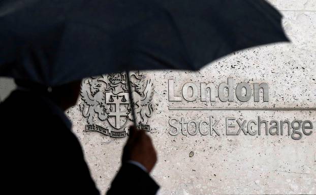 FILE PHOTO: A man shelters under an umbrella as he walks past the London Stock Exchange