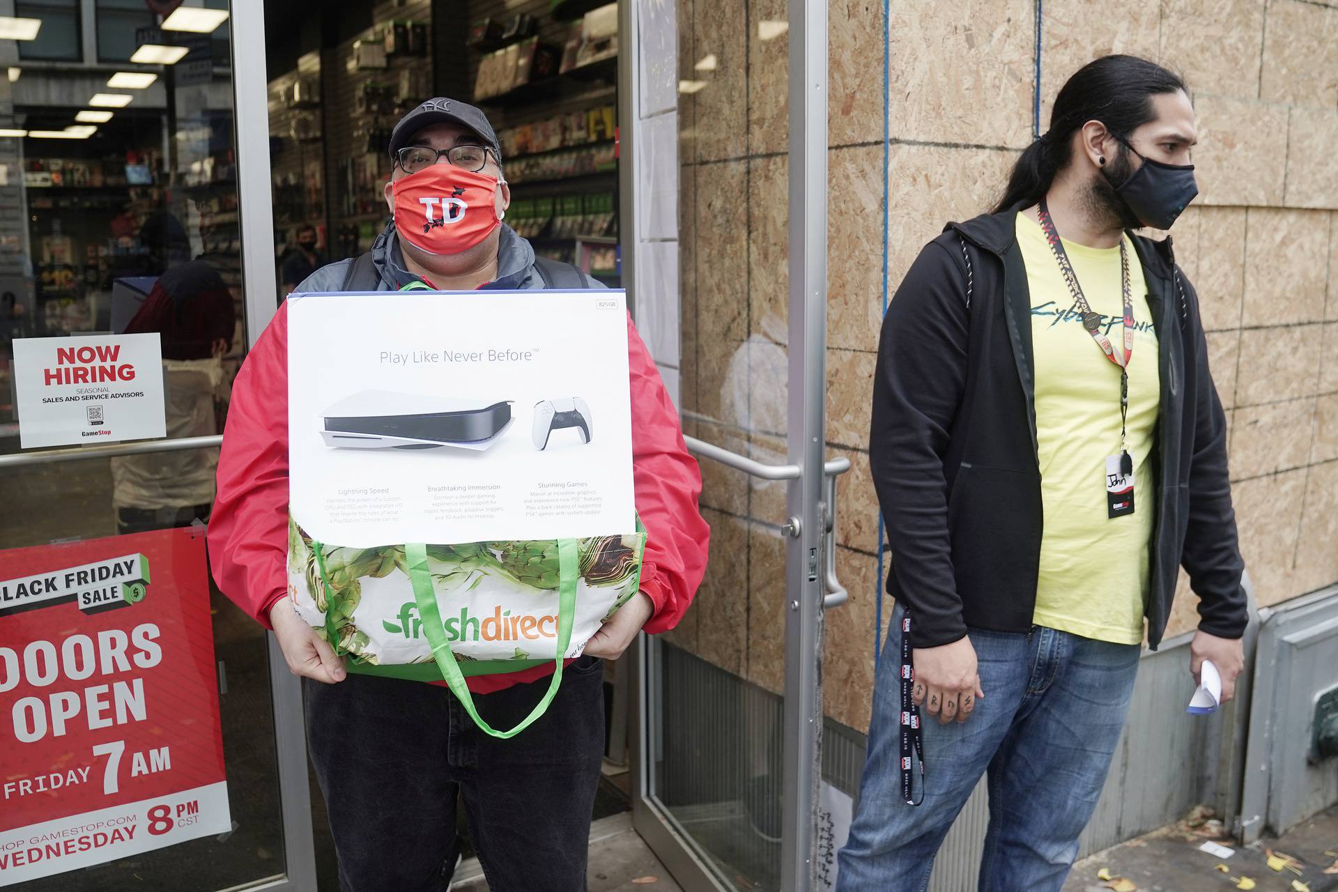 A man poses outside a GameStop store with his purchase of a Sony PS5 gaming console