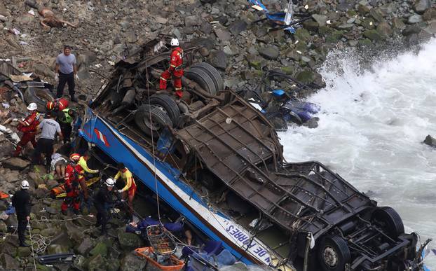 Rescue workers work at the scene after a bus crashed with a truck and careened off a cliff along a sharply curving highway north of Lima