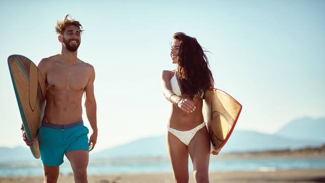 fit, sexy, young  couple walking and talking on beach, holding s