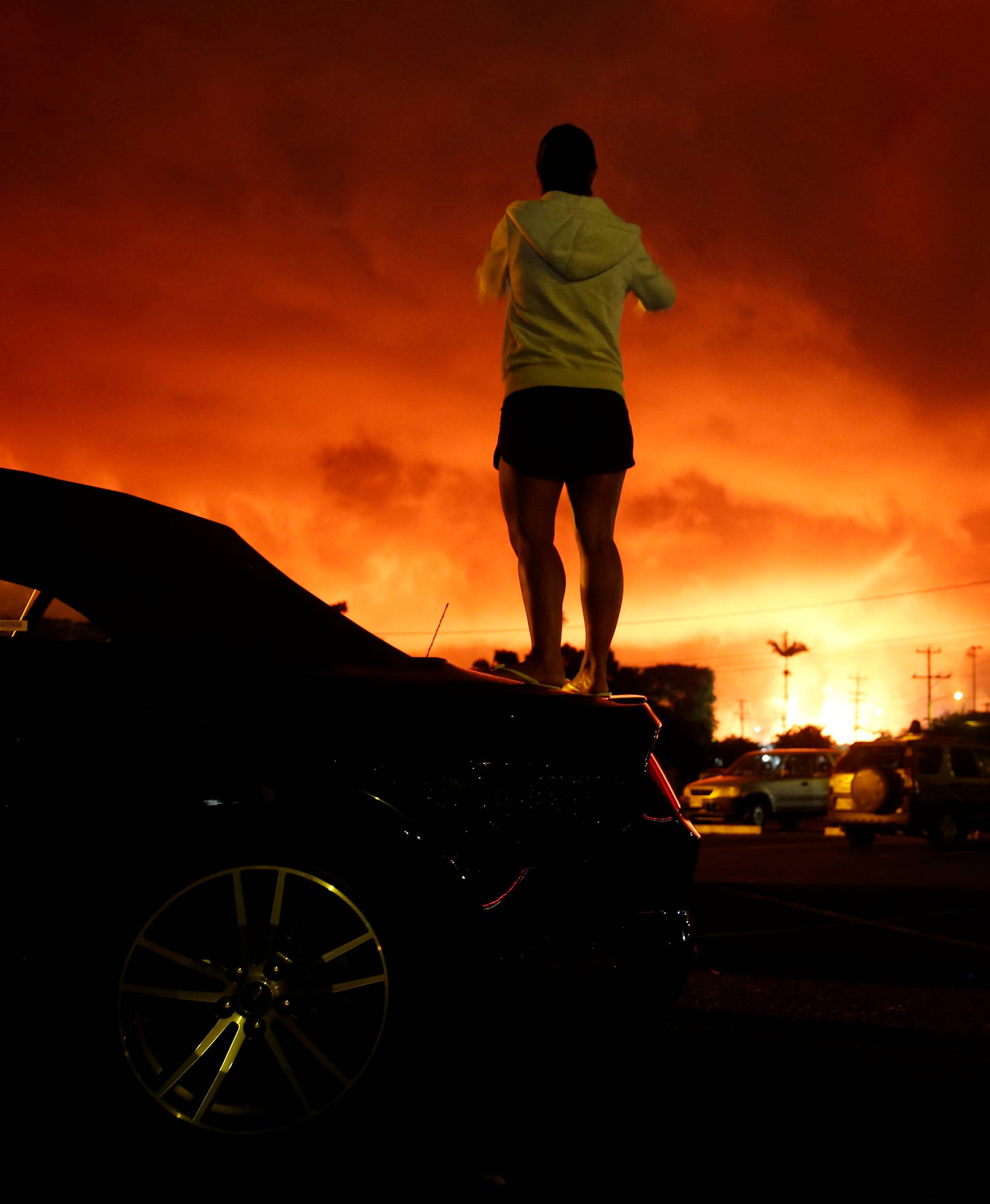 A woman takes a photo as lava lights up the sky above Pahoa