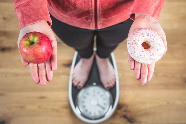 Healthy young woman looking at healthy and unhealthy plates of food, trying to make the right choice 