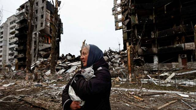 A woman carries her cat as she walks past buildings that were destroyed by Russian shelling