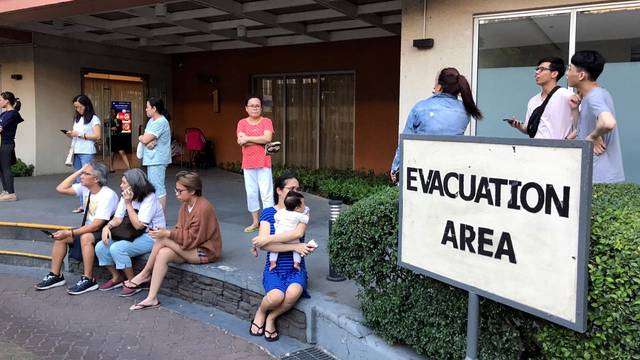 Residents sit outside after being evacuated from the condominium building after an earthquake in Makati City