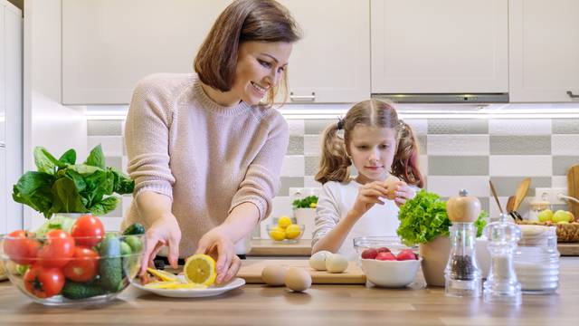 Smiling mother and daughter 8, 9 years old cooking together in kitchen vegetable salad. Healthy home food, communication parent and child.