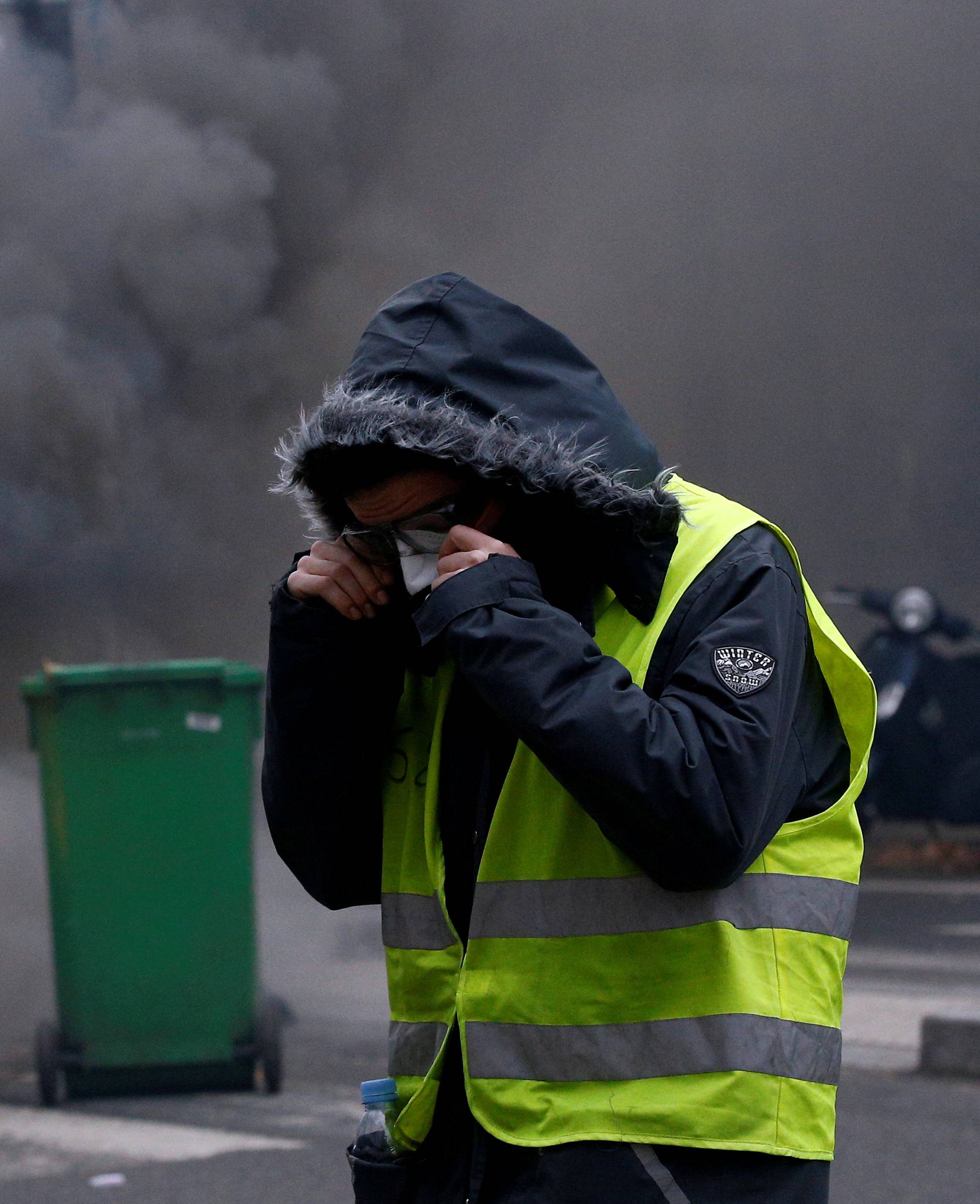 A protester wearing a yellow vest stands next to burning trash bins in a street during a national day of protest by the "yellow vests" movement in Paris