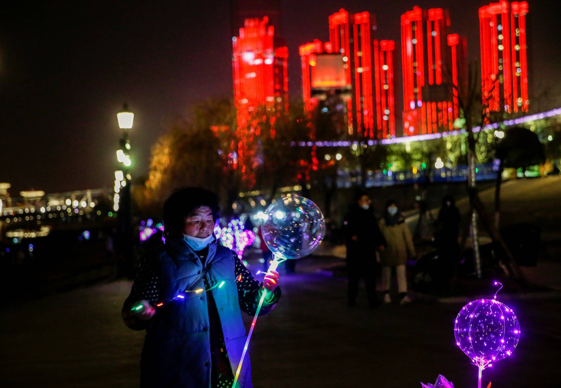Vendor decorates a balloon for sale by a river on New Year's Eve in Wuhan