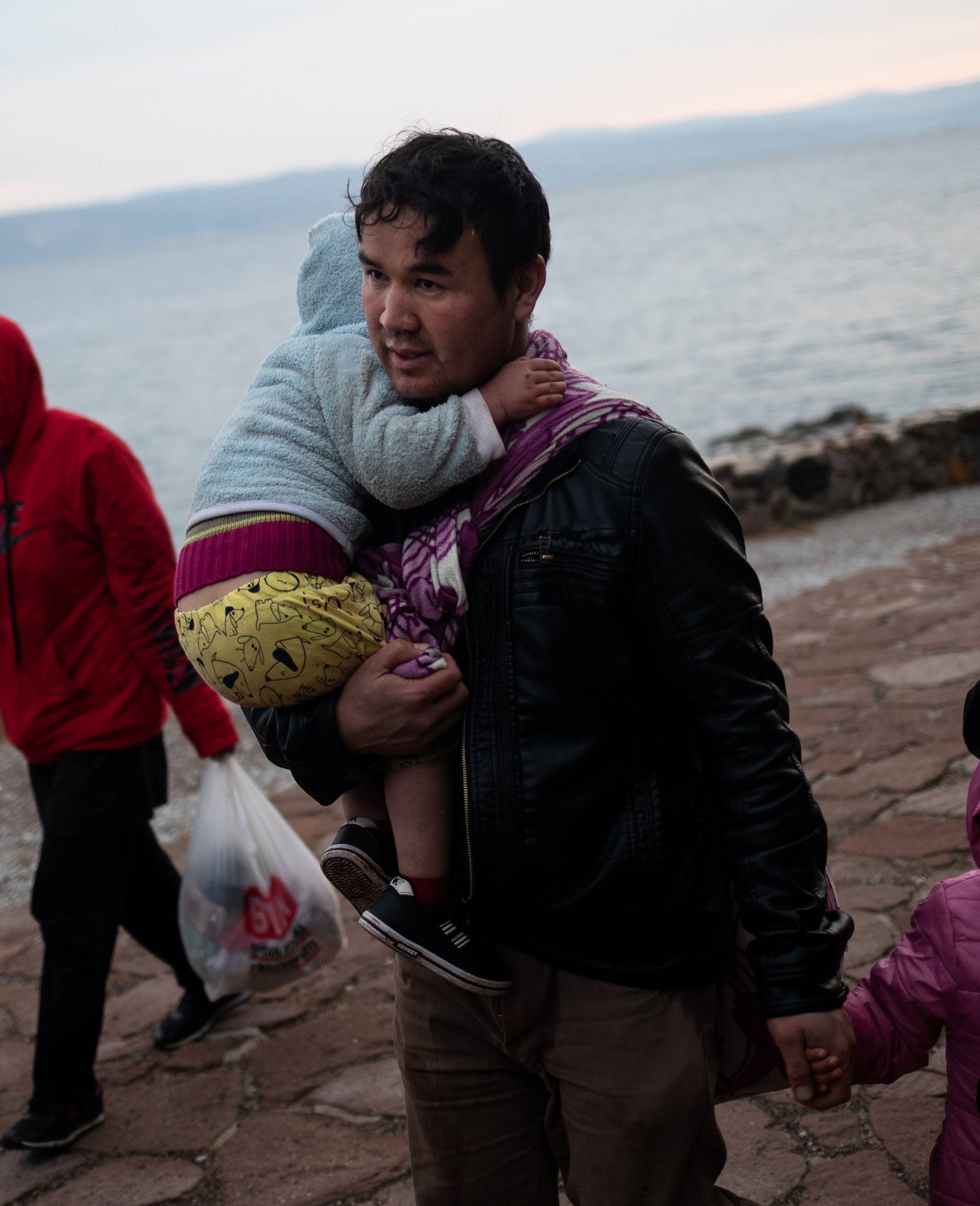 A man holds two children as migrants from Afghanistan arrive on a beach, after crossing part of the Aegean Sea from Turkey to the island of Lesbos