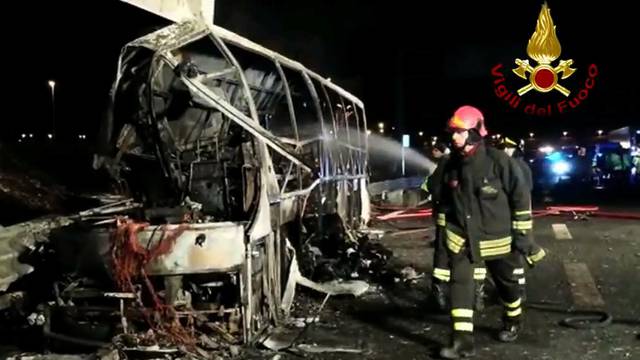 A still image taken from a video shows firefighters working next to a charred bus, which was carrying Hungarian students, on a side of a highway, near Verona