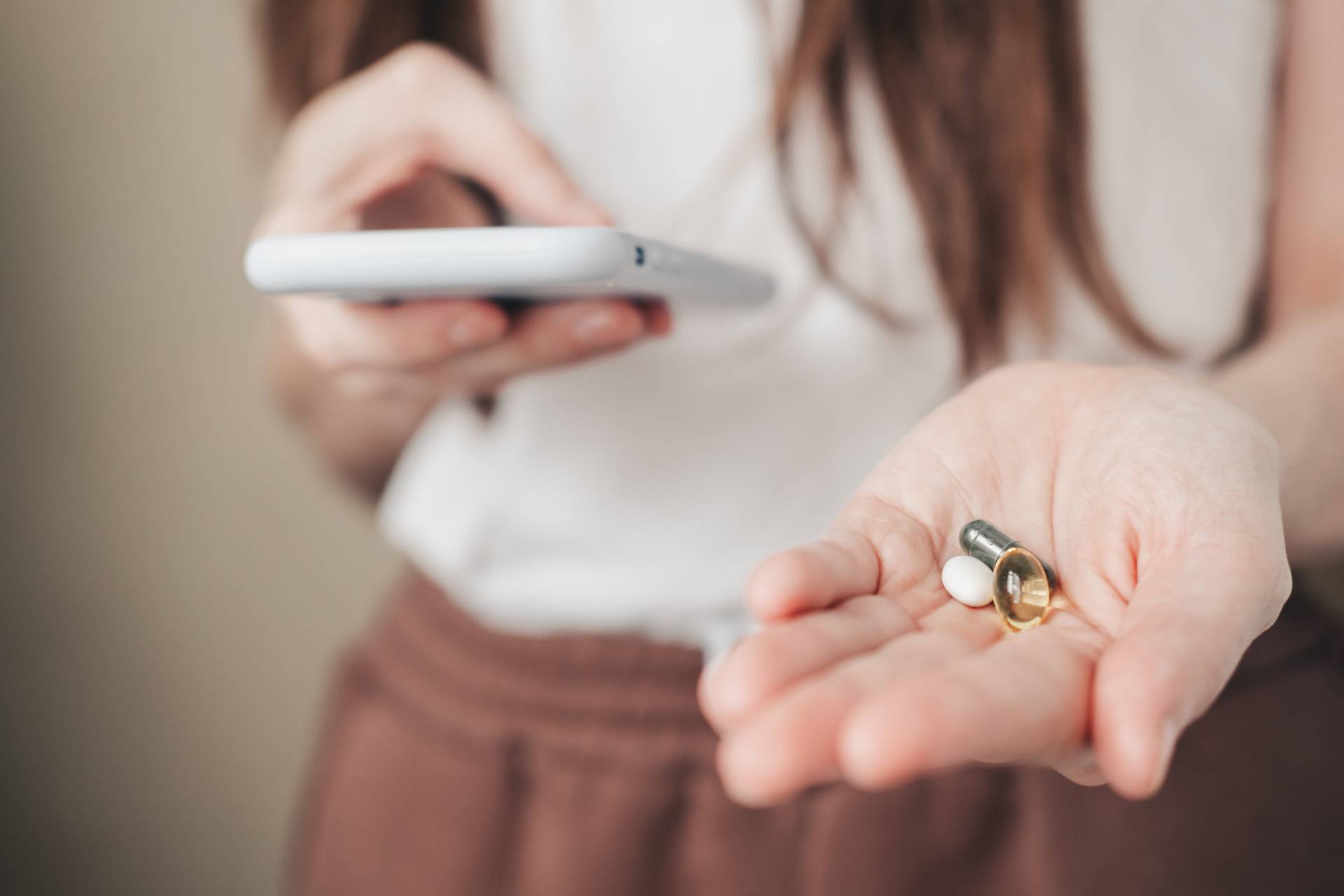 Vitamins for every day and a phone in the hands of the girl. spirulina, fish oil and magnesium in hands.