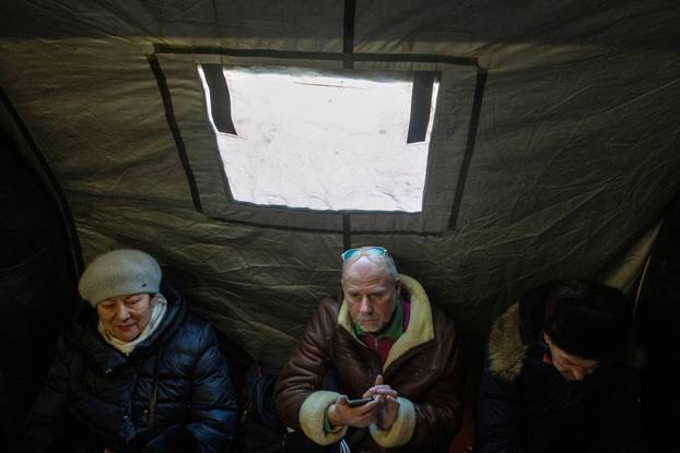 People warm up in a tent provided by emergency services for residents whose apartments are left without heating in Kyiv