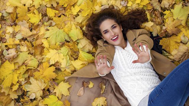 Young beautiful girl in blue jeans lying on yellow leaves