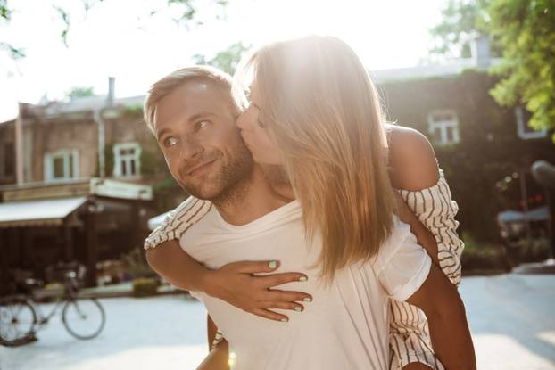Young beautiful couple smiling, kissing, embracing, walking in park.