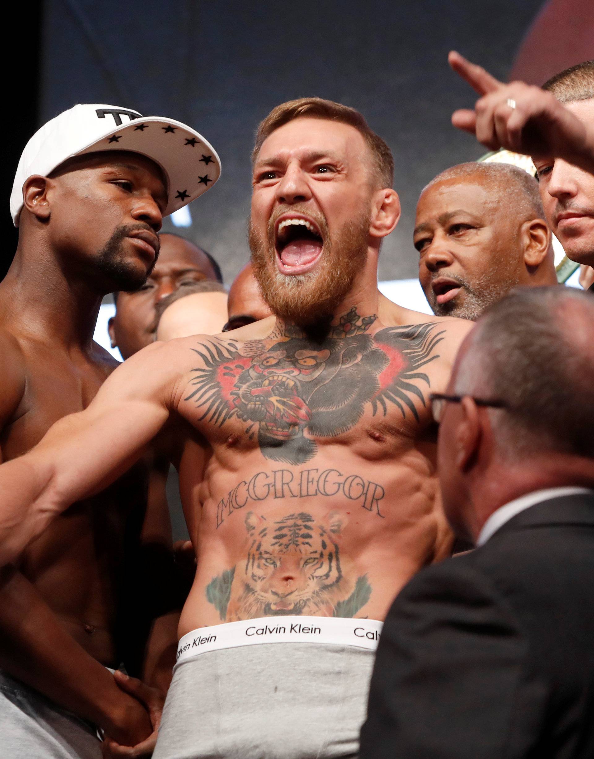 UFC lightweight champion Conor McGregor (C) of Ireland calls out as he poses with undefeated boxer Floyd Mayweather Jr. (L) of the U.S. during their official weigh-in at T-Mobile Arena in Las Vegas