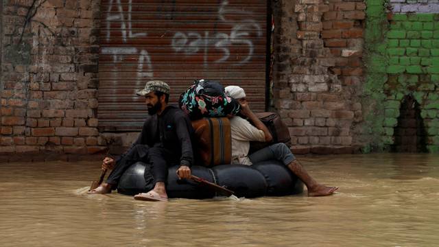 A volunteer paddles an inflatable tube as he evacuates a flood victim with his belongings, following rains and floods during the monsoon season in Charsadda
