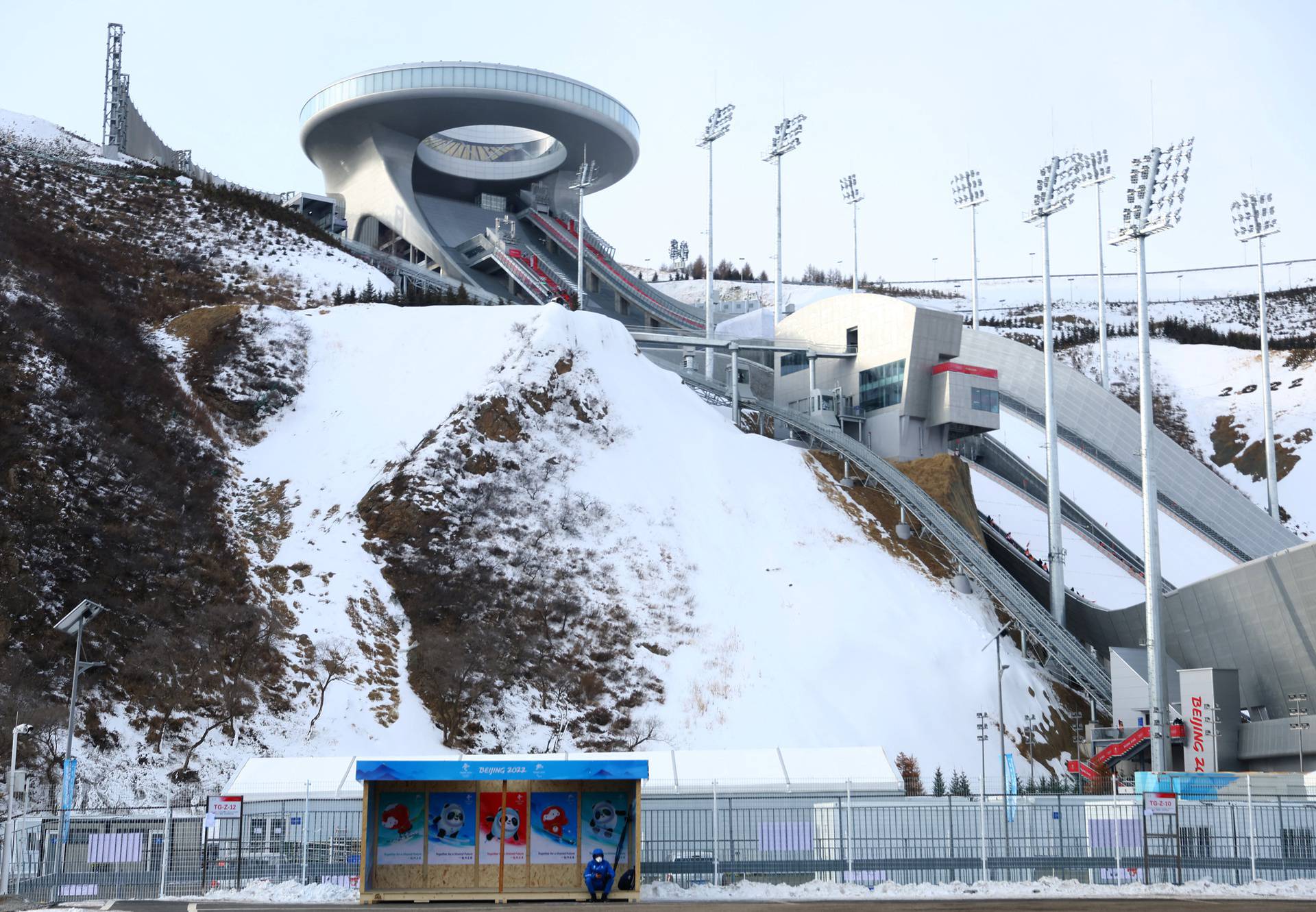 Person waits at a bus stop in front of the National Ski Jumping Center during the Beijing 2022 Winter Olympics