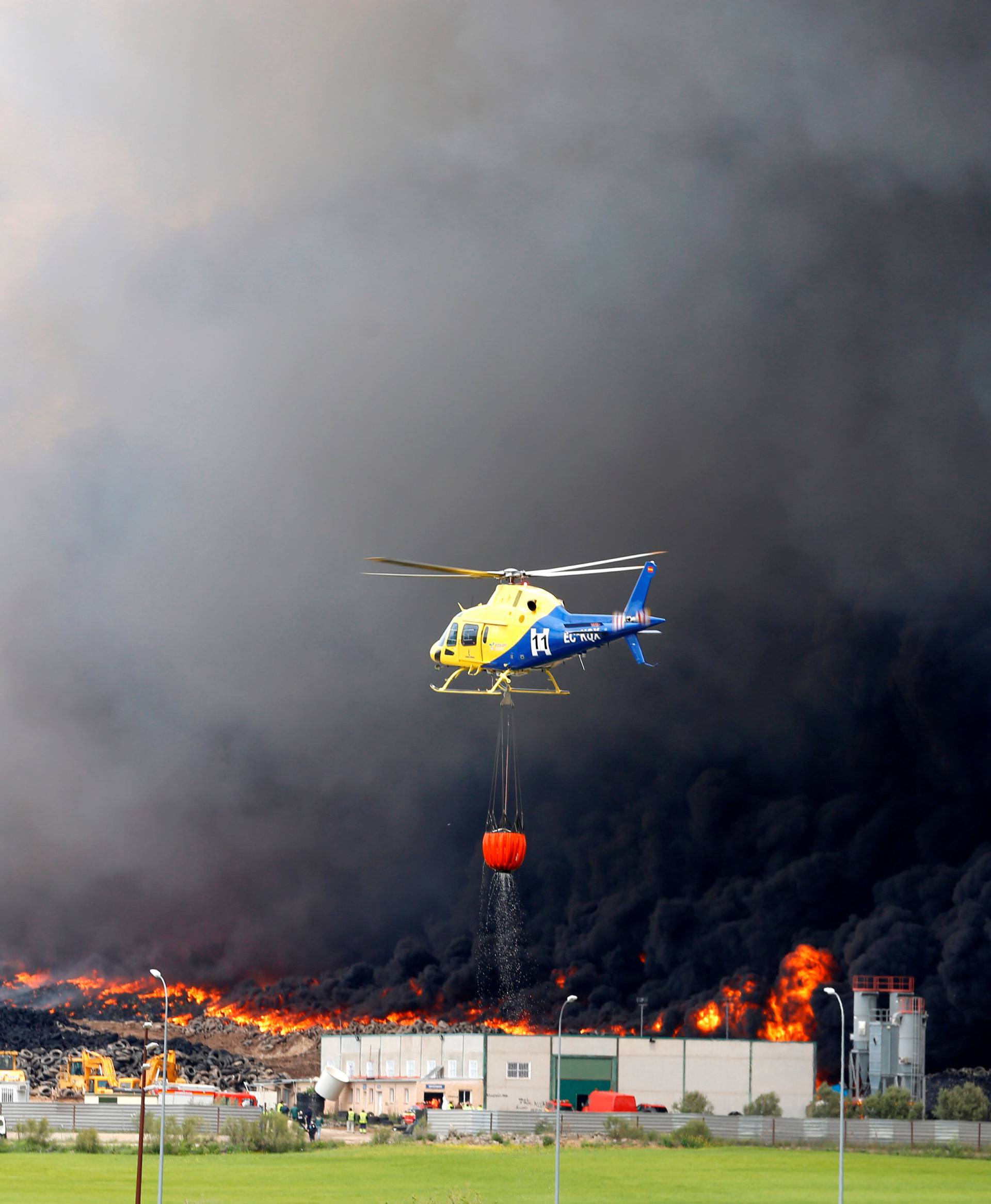 An helicopters prepares to throws water over a fire at a tyre dump near a residential development in Sesena