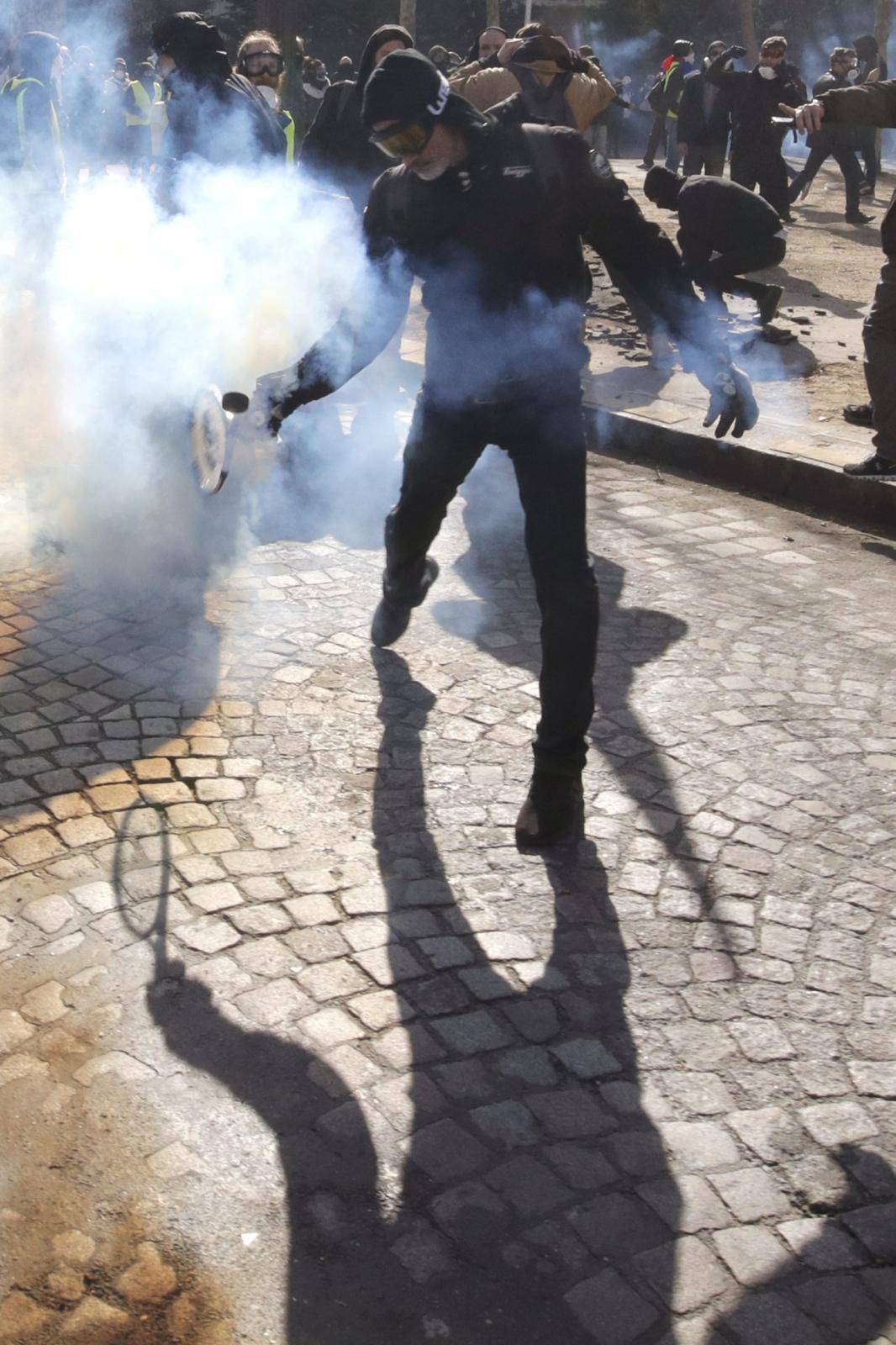 Protester throws back tear gas canister during demonstration by "yellow vests" in Paris
