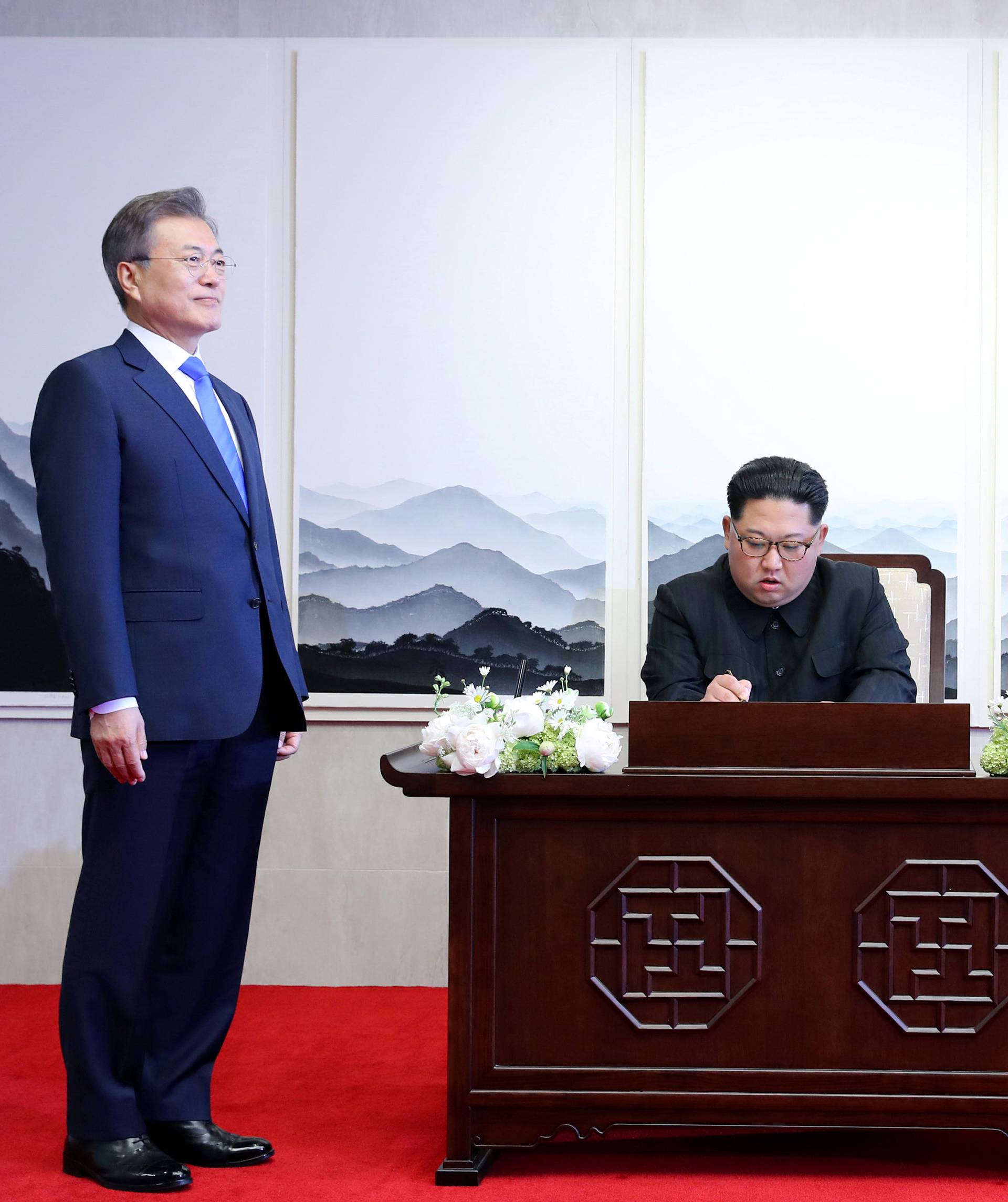 South Korean President Moon Jae-in watches as North Korean leader Kim Jong Un writes in a guestbook during their meeting at the Peace House