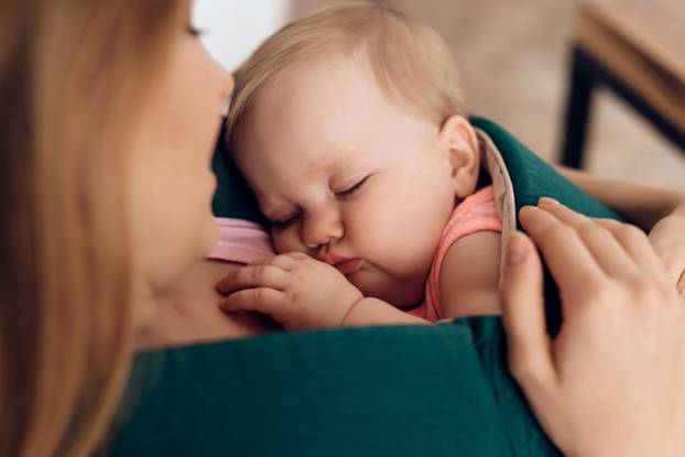 Young mother holding sleeping baby in baby sling.