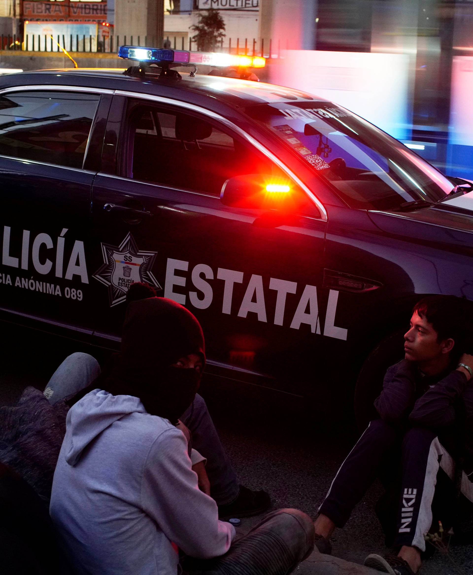 Migrant Nery Josvel from Honduras sits beside a police car as he waits for transportation during his journey towards the United States, in Mexico City