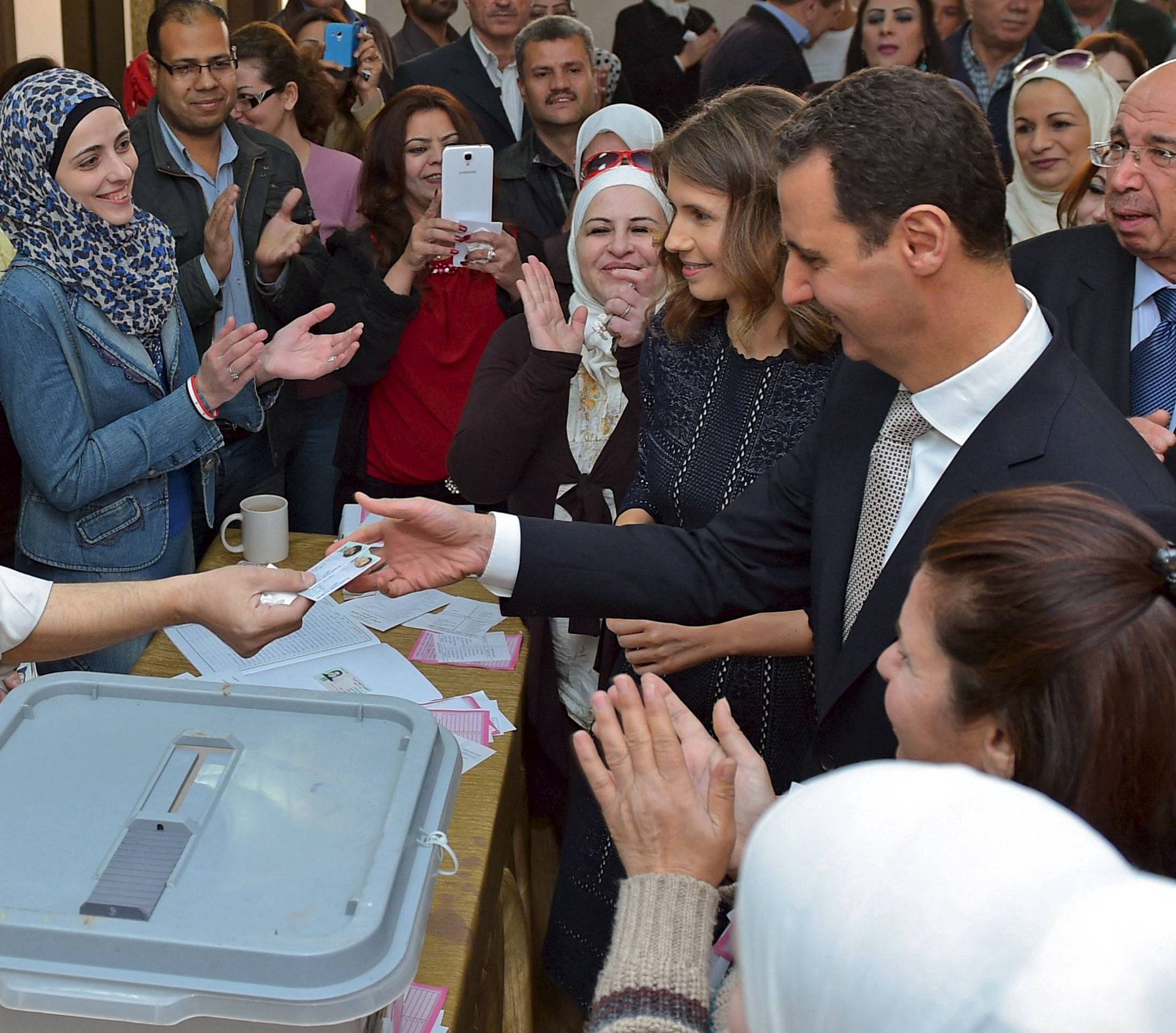 Syria's President Bashar al-Assad receives his Identification card next to his wife Asma after casting their votes, inside a polling station during parliamentary elections in Damascus