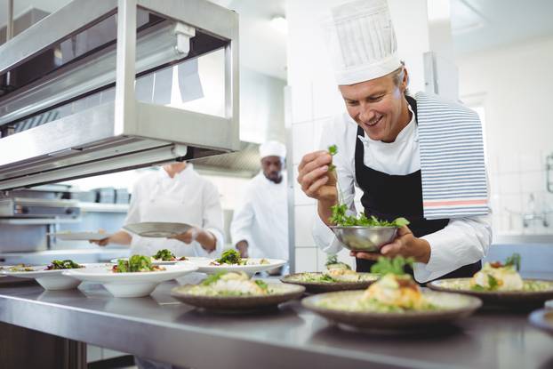 Happy chef garnishing appetizer plates at order station