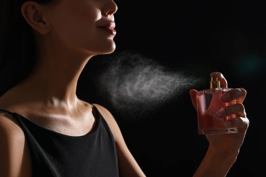 Woman spraying perfume on black background, closeup