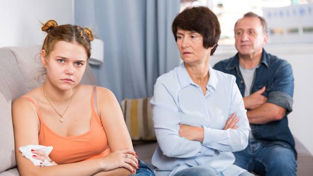 Adult couple is carefully talking with a sad daughter on sofa