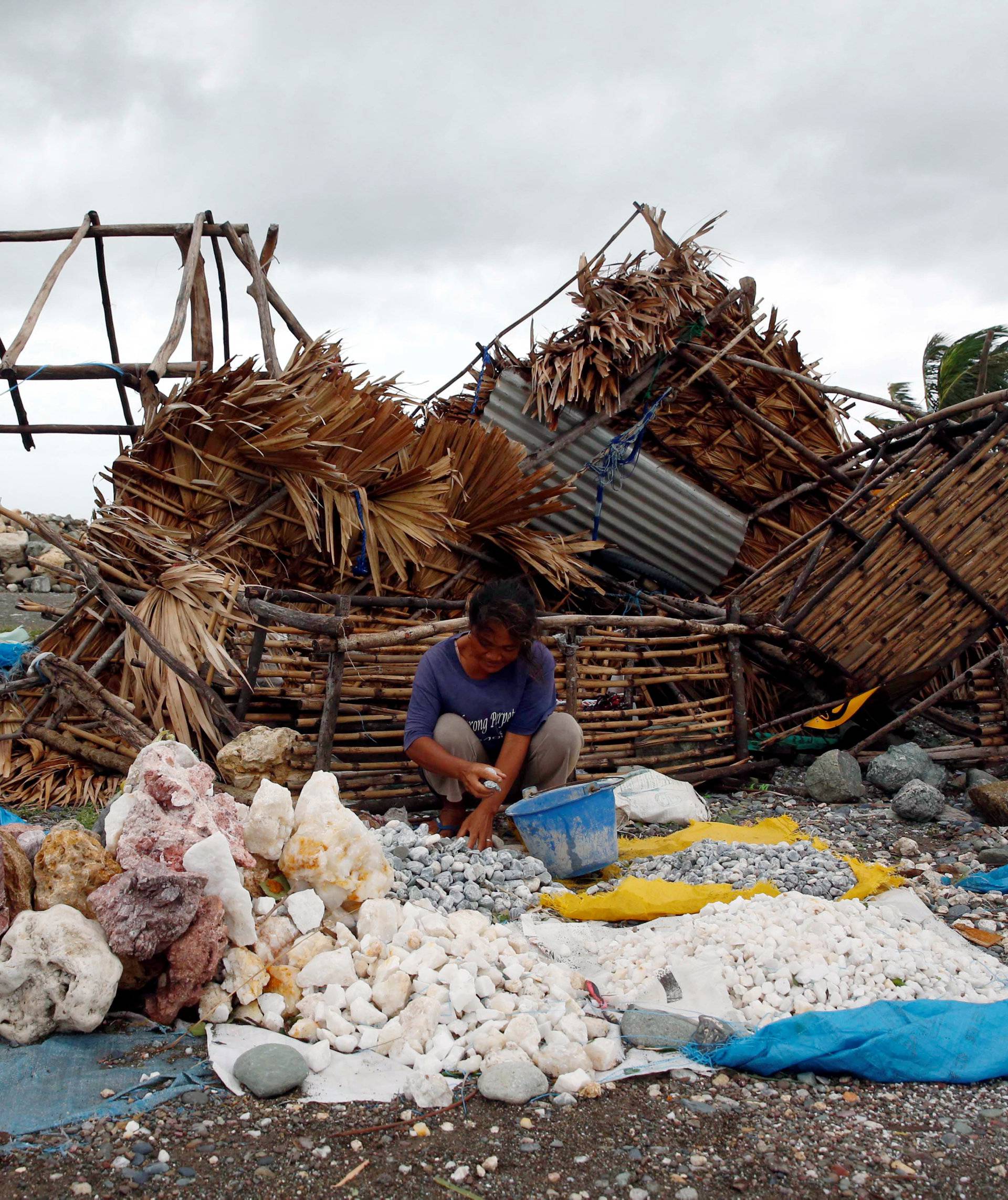 A woman sorts decorative rocks outside her shop toppled during Typhoon Haima, in Pasuiquin, Ilocos Norte