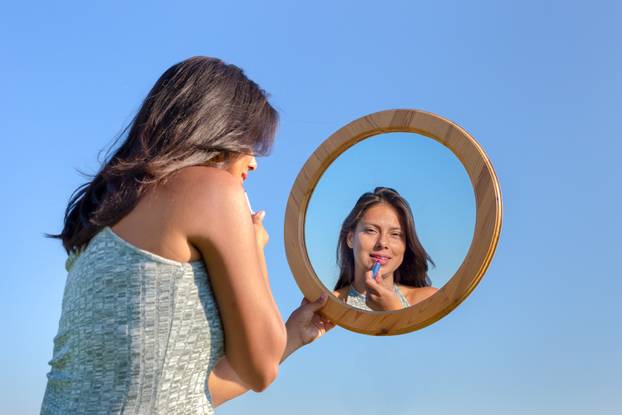 Woman applying lipstick makeup in mirror outside