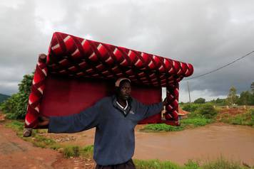 A man carries a sofa as he evacuates from his home after River Nzoia burst its banks and due to the backflow  from Lake Victoria, in Nyadorera, Siaya County