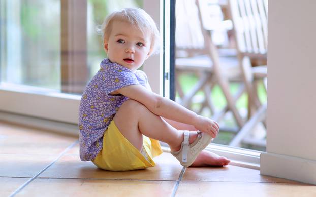 Toddler girl putting shoes sitting on floor next to window