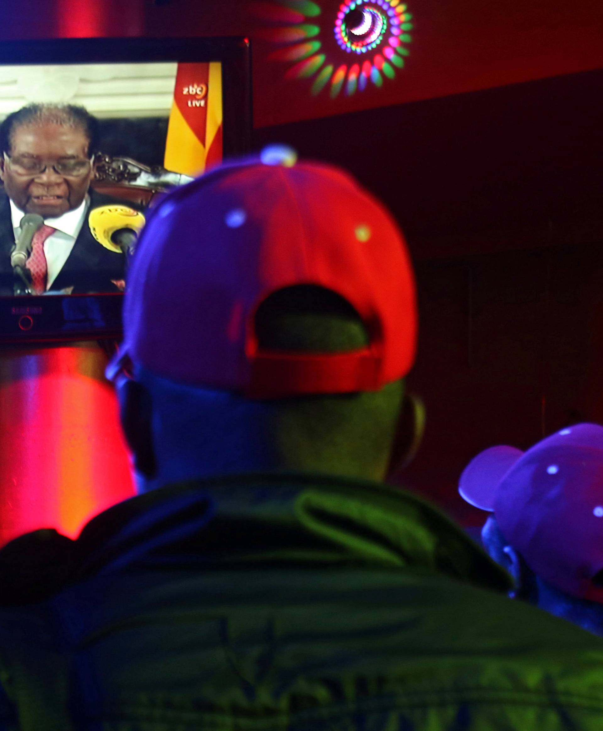 People watch as Zimbabwean President Robert Mugabe addresses the nation on television, at a bar in Harare
