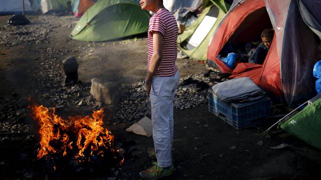 Boy warms up at a fire at a makeshift camp for migrants and refugees at the Greek-Macedonian border near the village of Idomeni