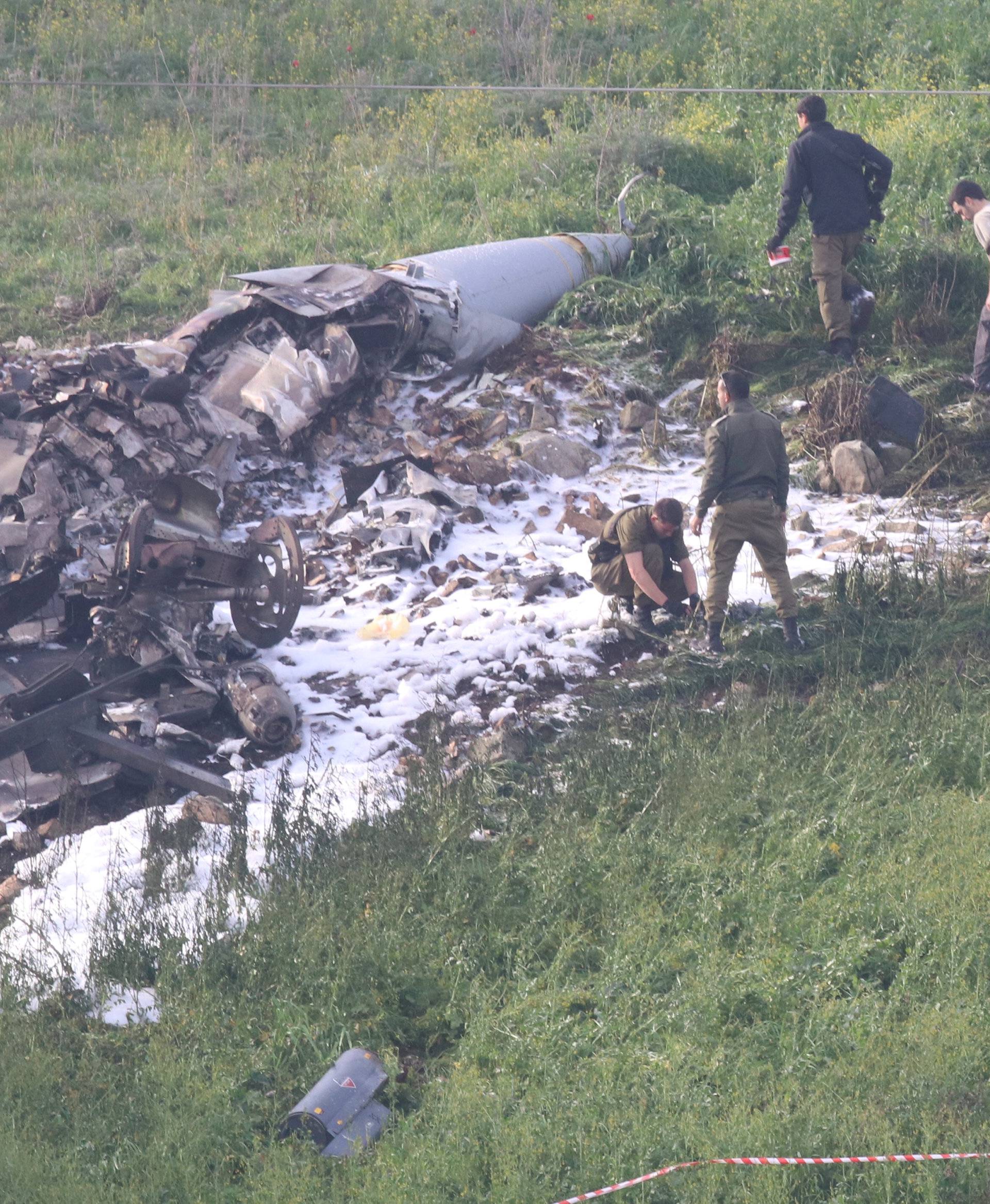 Israeli security forces walk next to the remains of an F-16 Israeli war plane near the Israeli village of Harduf