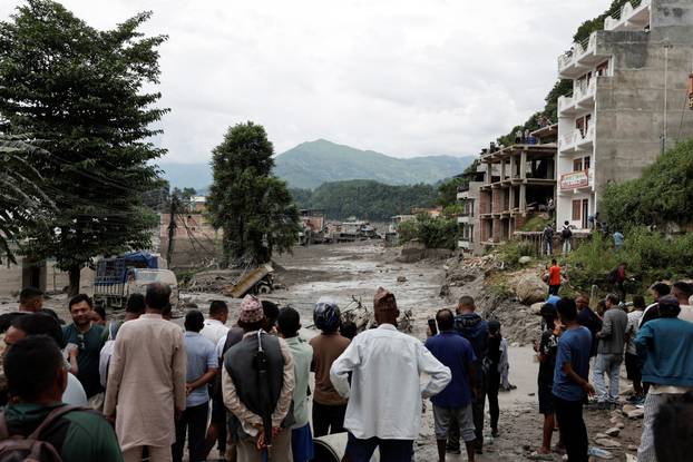 People stand near mud covered houses and a road, following a flash flood at Trishuli, Nepal