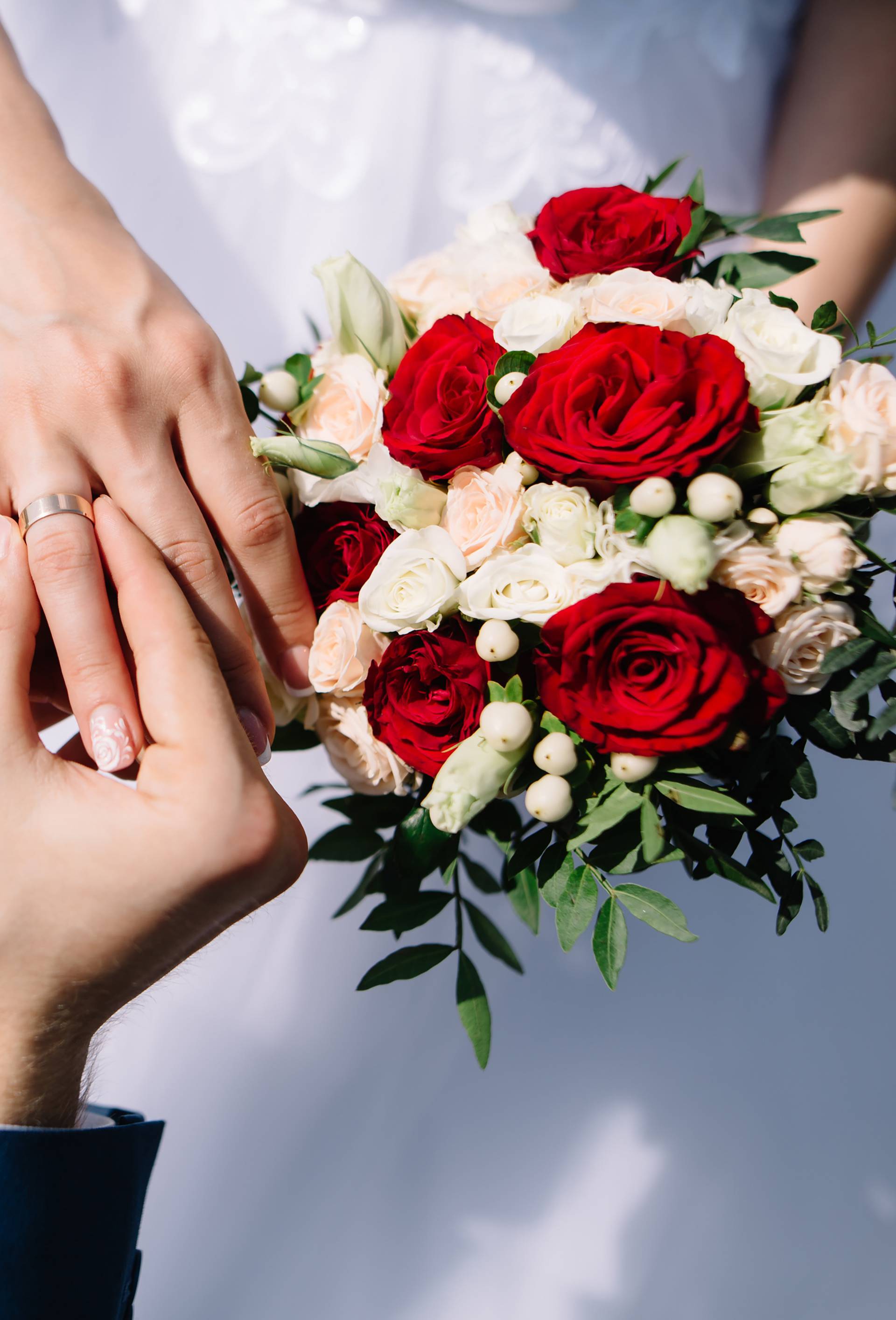 Love and marriage. Fine art rustic wedding ceremony outside. Groom putting golden ring on the bride's finger. Bouquet of red and white roses in hands