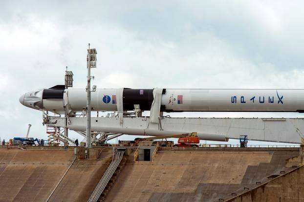 Crews work on the SpaceX Crew Dragon, attached to a Falcon 9 booster rocket, as it sits horizontal on Pad39A