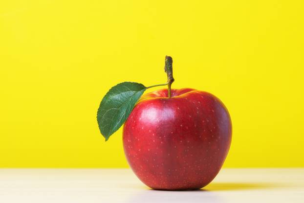 Red fresh apple with leaf against yellow background
