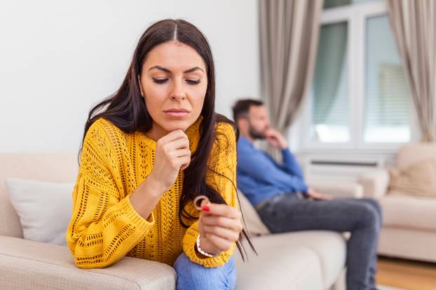 Stressed wife holding her wedding ring worried about breakup or divorce, avoid talking with husband after fight, anxious couple ignore each other. Frustrated sad wife taking off the wedding ring