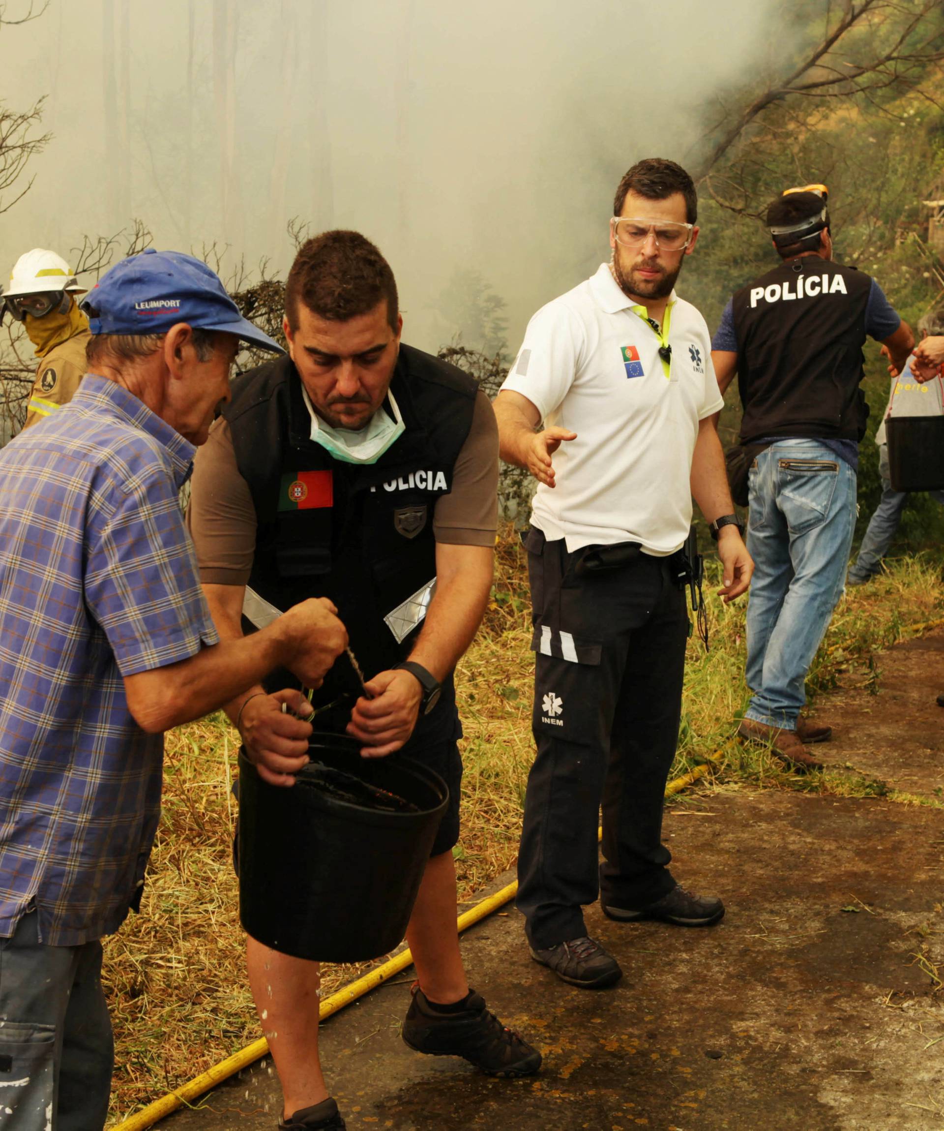 Civilians, and police officers pass water buckets to help extinguish a forest fire near houses at Sao Joao Latrao, Funchal, Madeira island