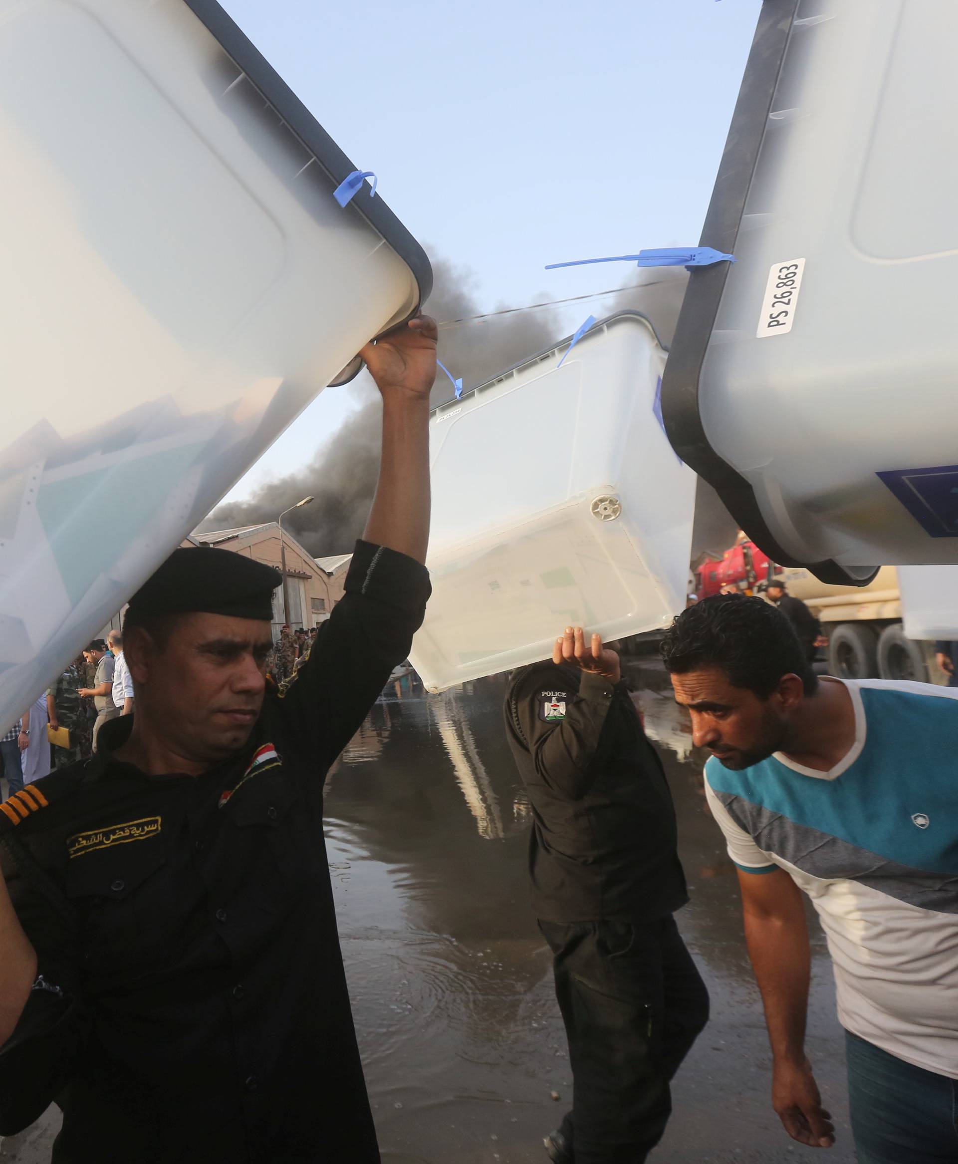 Security forces carry ballot boxes as smoke rises from a storage site in Baghdad, housing the boxes from Iraq's May parliamentary election