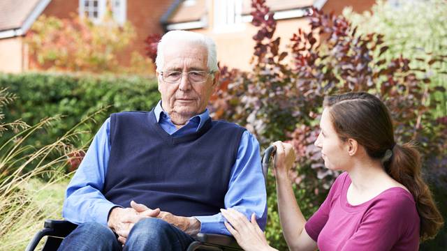 Adult Daughter Comforting Senior Father In Wheelchair