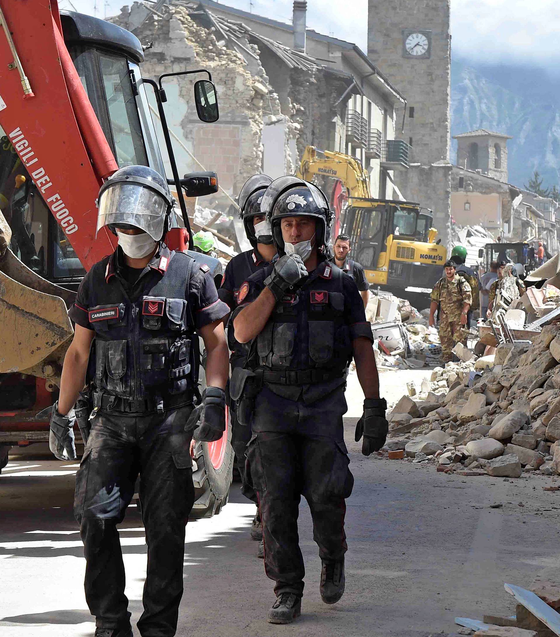 Rescuers walk next to collapsed buildings following an earthquake in Amatrice