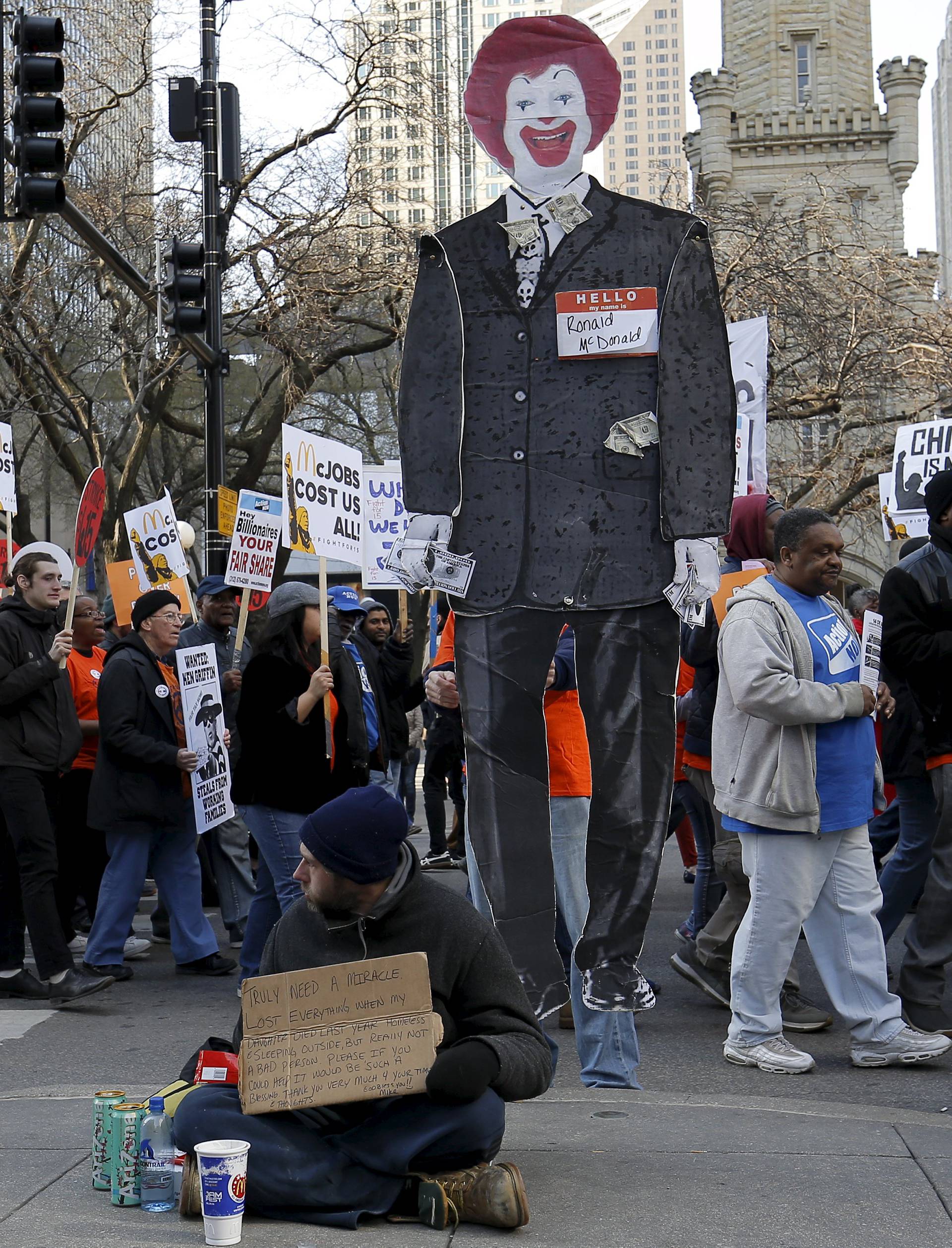 Protesters carrying a cutout of McDonald's character Ronald McDonald march past a homeless person during a demonstration calling for a $15-an-hour nationwide minimum wage in downtown Chicago